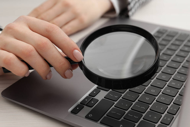Woman holding magnifier near laptop at wooden table, closeup. Online searching concept - Valokuva, kuva