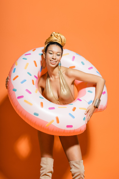Overjoyed african american woman in swimsuit holding pool ring on orange background  - Foto, Imagen