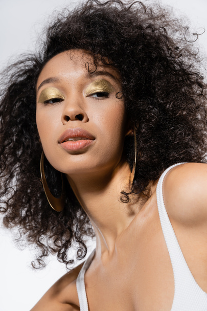 portrait of curly african american woman with golden eye shadows looking away isolated on grey  - Photo, Image