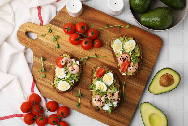 Deliciosos sándwiches con guacamole, camarones y tomates sobre mesa blanca, puesta plana - Foto, Imagen