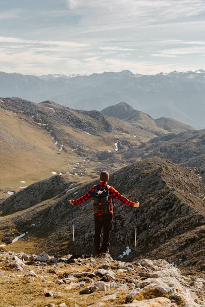 альпинист в красной одежде, рюкзак и пешеходные палки созерцает пейзаж с горной вершины. открытый спорт и приключения - Фото, изображение