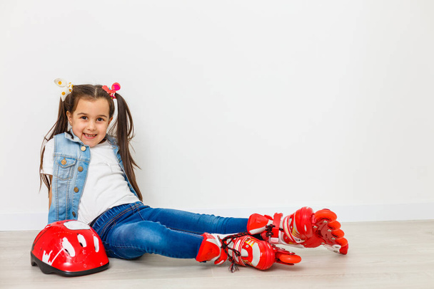 Щаслива маленька дівчинка з роликовими ковзанами та захисним спорядженням відпочиває ізольована
 - Фото, зображення