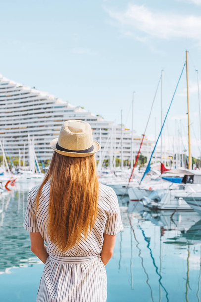 Ξανθά μαλλιά γυναίκα σε ένα καπέλο στέκεται με την πλάτη της στη θάλασσα, γιοτ και βάρκες φόντο. Διακοπές στην Ευρώπη. Ωραία, Γαλλική Ριβιέρα. Ταξιδιωτική φωτογραφία. - Φωτογραφία, εικόνα