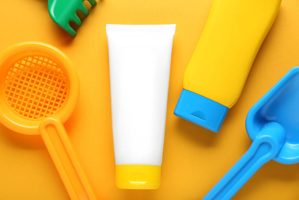 Different suntan products and plastic beach toys on orange background, flat lay - Foto, Bild