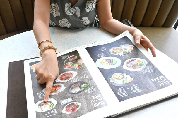Woman finger point with menu choosing ordering dishes at restaurant. Menu has thai language with English translation. - Photo, Image