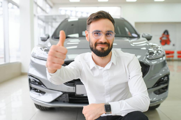 Happy young guy checking new luxury car, buying automobile at dealership centre. Portrait of cheerful millennial Caucasian man examining auto at showroom store. - Fotó, kép