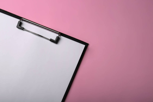 Black clipboard with sheet of blank paper on pink background, top view. Space for text - Фото, зображення