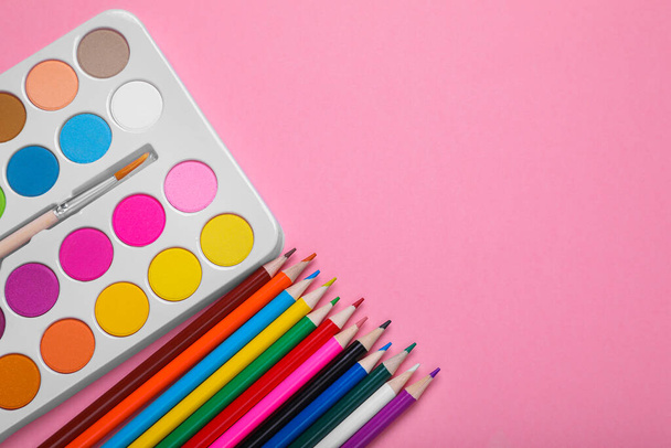 Watercolor palette with brush and colorful pencils on pink background, flat lay. Space for text - Fotoğraf, Görsel