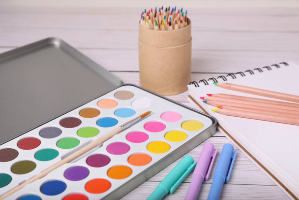 Watercolor palette with brush, pencils, markers and notebook on white wooden table, closeup - Foto, immagini
