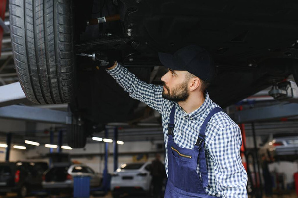 Portrait of a mechanic repairing a lifted car. - Fotoğraf, Görsel