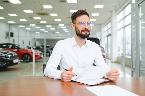 Confident young caucasian businessman shop assistant receptionist working writing at reception desk in car automobile dealer shop. - Photo, image
