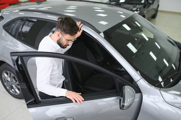 a man examines a car in a car dealership. - 写真・画像