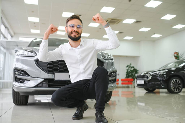 Happy young guy checking new luxury car, buying automobile at dealership centre. Portrait of cheerful millennial Caucasian man examining auto at showroom store. - Foto, afbeelding