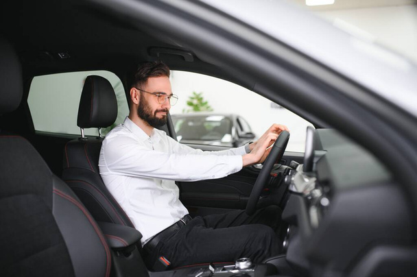 Happy young guy checking new luxury car, buying automobile at dealership centre. Portrait of cheerful millennial Caucasian man examining auto at showroom store. - Foto, Imagen
