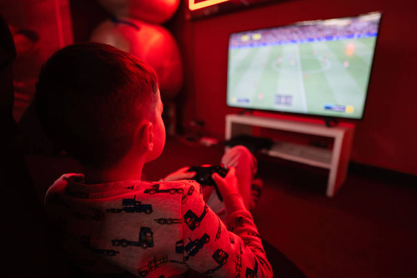 Boy gamer play gamepad football video game console in red gaming room. - Φωτογραφία, εικόνα