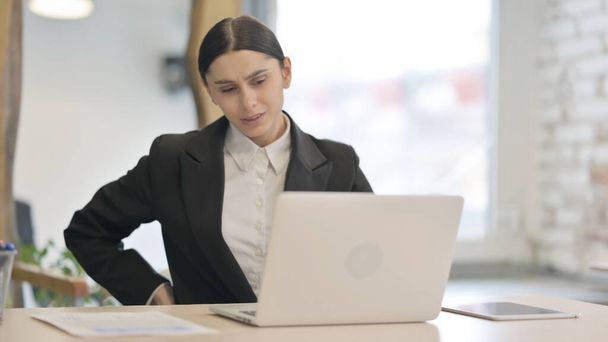 Junge Geschäftsfrau mit Rückenschmerzen arbeitet am Laptop - Foto, Bild