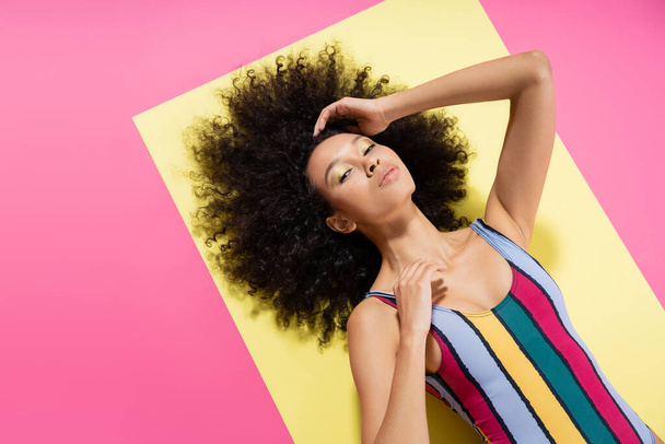 top view of curly african american woman in colorful swimsuit lying on yellow and pink background  - Φωτογραφία, εικόνα