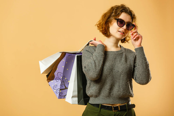 Porträt eines aufgeregten schönen Mädchens mit Sonnenbrille, das Einkaufstüten isoliert vor beigem Hintergrund hält. - Foto, Bild