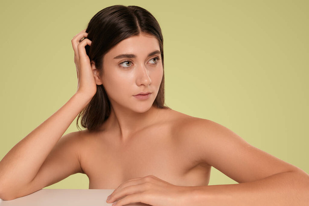 Natural young female with bare shoulders and long hair wearing no makeup on clean face and looking away on green background - Фото, изображение