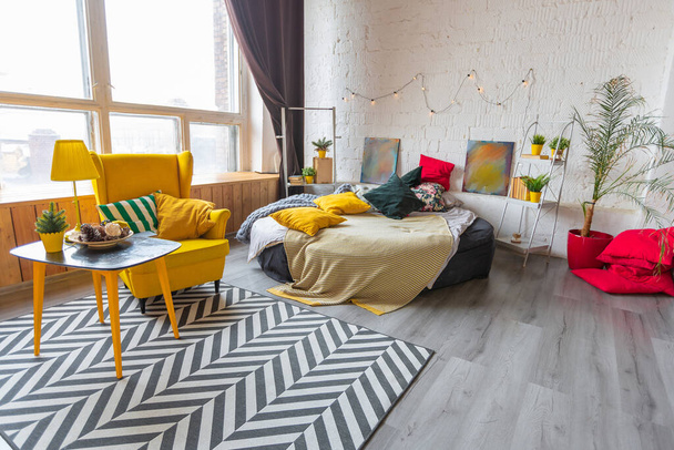 Trendy fashion luxury interior design in Scandinavian style of studio apartment with bright yellow furniture and decorated with new year lights. - Фото, изображение