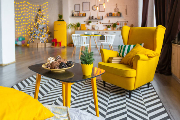 Trendy fashion luxury interior design in Scandinavian style of studio apartment with bright yellow furniture and decorated with new year lights. - Фото, изображение