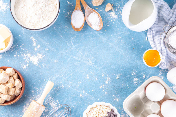 Baking ingredients background. Cooking ingredients (flour, eggs, milk, brown sugar, butter) with utensils on light blue background top view copy space - Фото, изображение