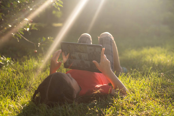 Девушка на траве с планшетным чатом в руках в саду. - Фото, изображение