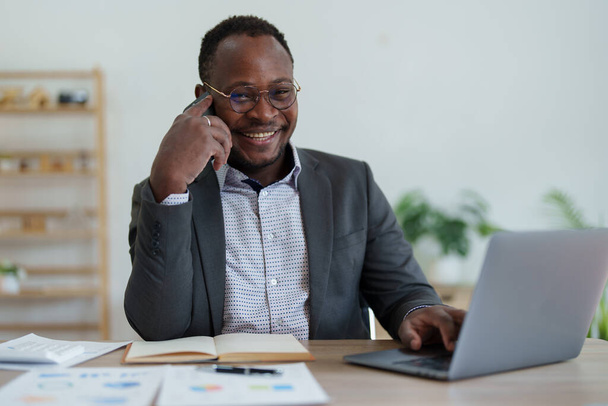 mężczyzna w średnim wieku American African za pomocą smartfona komórkowego i laptopa z planowaniem pracy nad dokumentem finansowym, podatkiem, wymiana, księgowość i doradztwo finansowe. - Zdjęcie, obraz