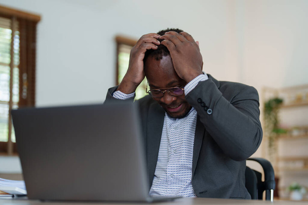 Burnout Amerykański afrykański biznesmen w stresie pracuje z wieloma dokumentami papierkowej roboty, atak migreny, Freelance, praca w domu. - Zdjęcie, obraz