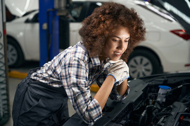 Smiling female auto mechanic inspecting a car under the hood, the car is being serviced - Foto, Bild