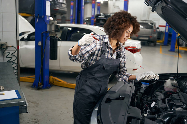 Multiracial young auto repairman checks oil level in car, woman works in comfortable work overalls - Zdjęcie, obraz