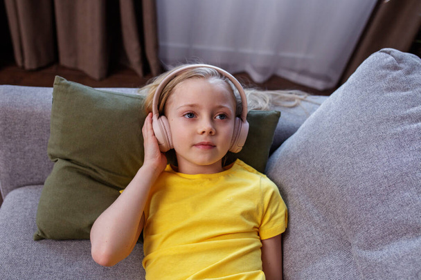 Happy child listens to music or audiobook. Little school kid wearing headphones. Music makes my day - 写真・画像
