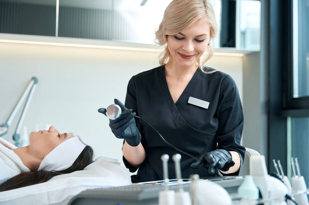 Cosmetologist in protective gloves sitting near the table with instruments and preparing for procedure - Photo, Image