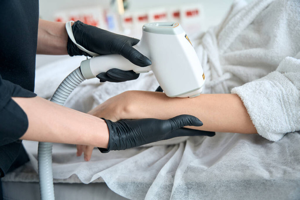 Female in protective gloves standing near adult lady and doing laser hair removal on the hand - Fotoğraf, Görsel