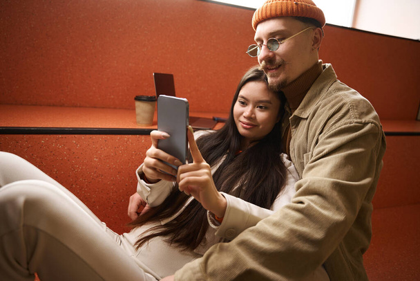 Pleased young Asian woman and smiling happy Caucasian man taking selfie indoors - Fotografie, Obrázek