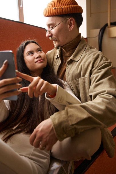 Loving guy hugging his smiling happy young woman with smartphone in hand - Foto, Imagen