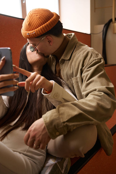 Female and male kissing on lips while taking selfie with mobile phone - Fotó, kép