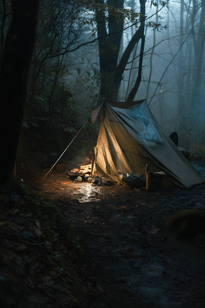 Überleben in der Wildnis: Bushcraft-Zelt unter der Plane bei starkem Regen, das die Kälte der Morgendämmerung aufnimmt - eine Szene der Ausdauer und Widerstandskraft - Foto, Bild