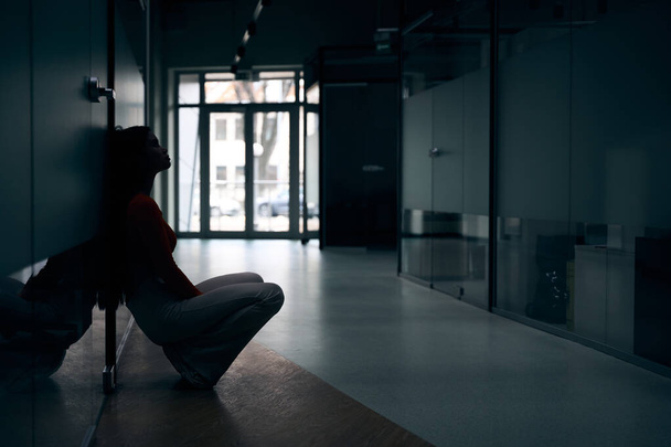 Vue latérale d'une travailleuse d'entreprise découragée assise sur ses hanches appuyée contre une porte fermée - Photo, image