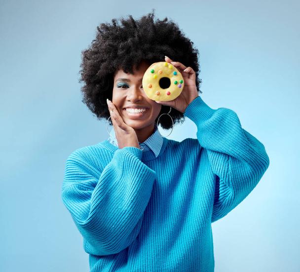Black woman, smile and donut with blue makeup against studio background. Model, happy and beauty with cake in hand by face show happiness against fashion backdrop with hair, skin and healthy teeth. - Фото, изображение