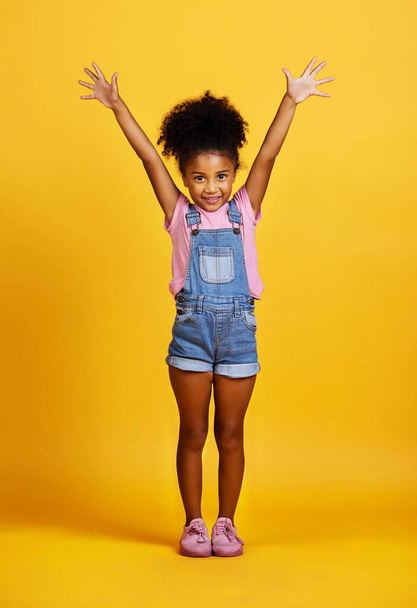 Studio, portrait and excited child with hands up and a smile on face on yellow background. Happy young girl kid model with happiness, carefree and positive attitude for surprise sale announcement. - Фото, изображение