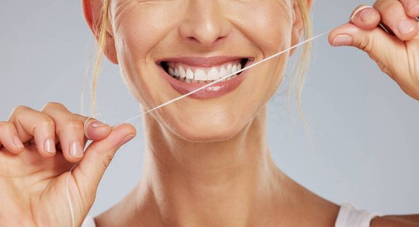 Zęby nici dentystycznej, wellness stomatologicznego i kobieta z uśmiechem podczas czyszczenia usta na szarym tle makiety studio. Ręce modelki ze sznurkiem do pielęgnacji zębów i ustnej opieki zdrowotnej z uśmiechem. - Zdjęcie, obraz