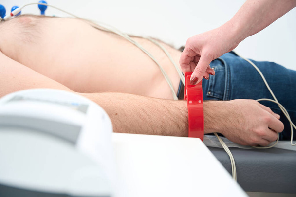 Foto ritagliata di elettrodi ECG sulla mano del paziente maschile. Elettrocardiogramma, procedura ECG in clinica medica - Foto, immagini