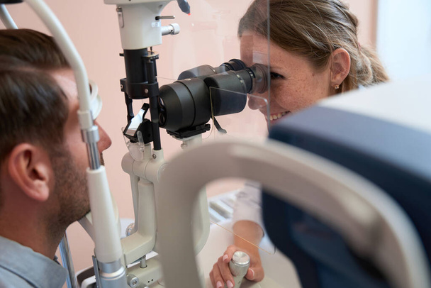 Close up vista laterale ritratto di donna medico qualificato sorridente sta guardando attraverso la lampada a fessura durante l'esame acuità visiva nel mobile medico - Foto, immagini