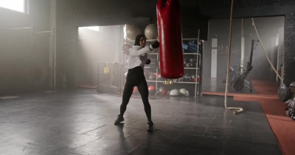 Belle femme caucasienne faisant des exercices de boxe dans la salle de gym. Charmante femme avec des bandages de mains poinçonnant sac de boxe, l'entraînement intensivement seul. Concept de corps sain et fort. - Séquence, vidéo