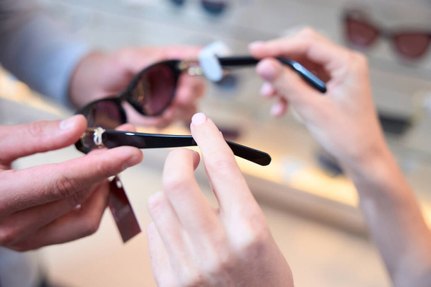 Imagen de cerca de las manos femeninas está mostrando las gafas de sol con estilo para el cliente en la tienda moderna - Foto, imagen