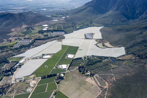 Luftaufnahme aus einem Segelflugzeug mit Weinbergen und landwirtschaftlichen Unterständen in der Landschaft am Fuße des Audensberg-Gebirges, aufgenommen von Südwesten bei hellem Sommerlicht in der Nähe von Worcester, Western Cape, Südafrika - Foto, Bild