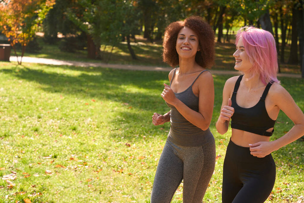Веселая молодая женщина и ее довольная подруга бегут через лужайку в парке - Фото, изображение