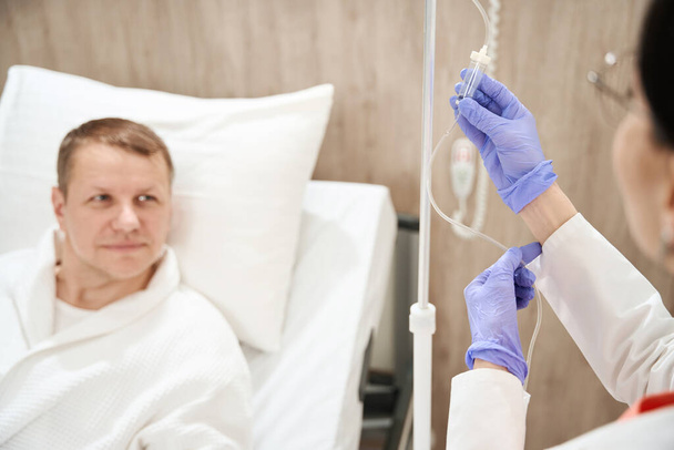 Abgeschnittener Kopf Porträt des Arztes Hände in Handschuhen bereitet Medizin für Mann Patient in moderner Klinik - Foto, Bild