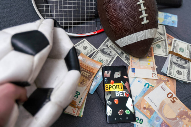 Zakłady sportowe online. Dolary spadają na tło dłoni ze smartfonem i piłką nożną. Twórcze pochodzenie, hazard - Zdjęcie, obraz